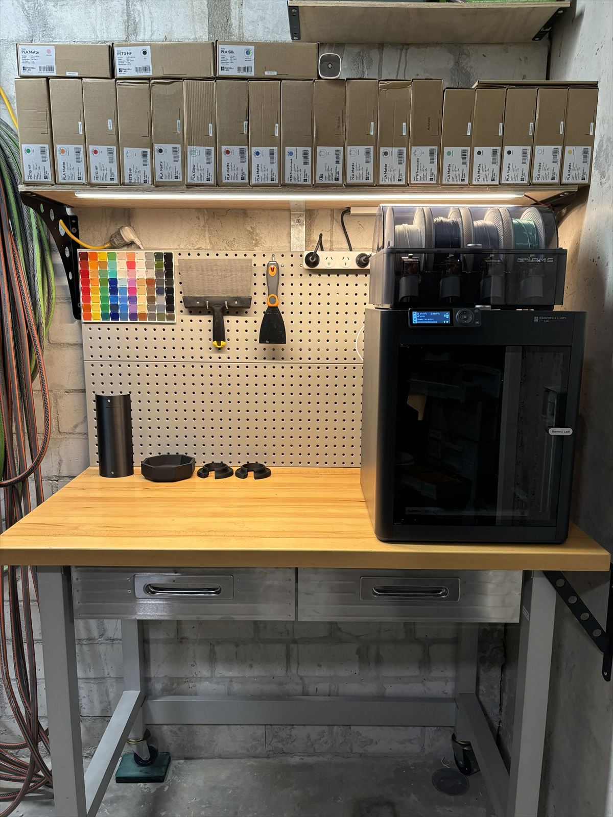 Bambu Lab P1S printer with AMS on the WITT workbench, filament stock on the shelf above